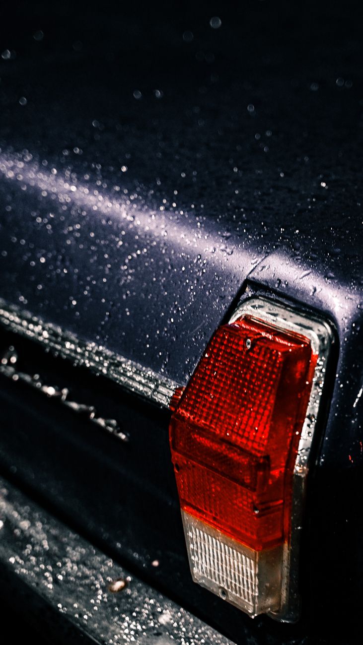 Detailed shot of a classic car's taillight covered in water droplets, showcasing vintage automotive design.