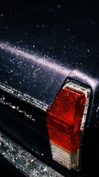 Detailed shot of a classic car's taillight covered in water droplets, showcasing vintage automotive design.
