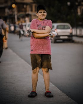 Young boy standing on the street holding pigeons in a lively urban setting.