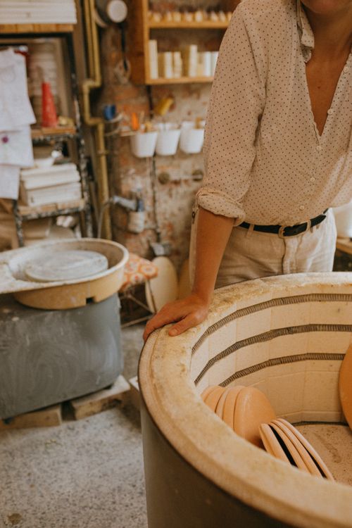 Free A dedicated artisan working in a pottery workshop with a kiln and various ceramic pieces on display. Stock Photo