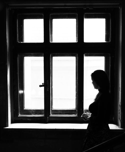Free Artistic black and white silhouette of a woman standing by a large window. Stock Photo