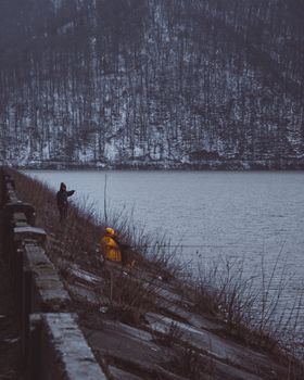 两个穿着外套的人靠在白雪皑皑的湖岸上进行冬季钓鱼