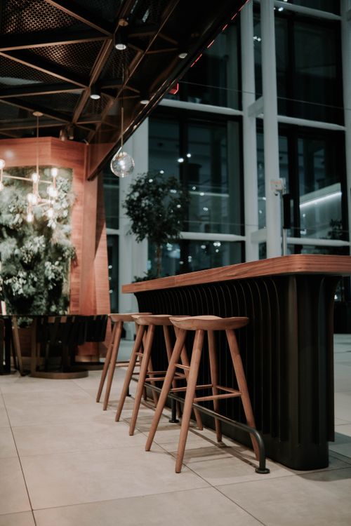 Free Stylish indoor café setting with wooden barstools and modern decor, featuring greenery. Stock Photo