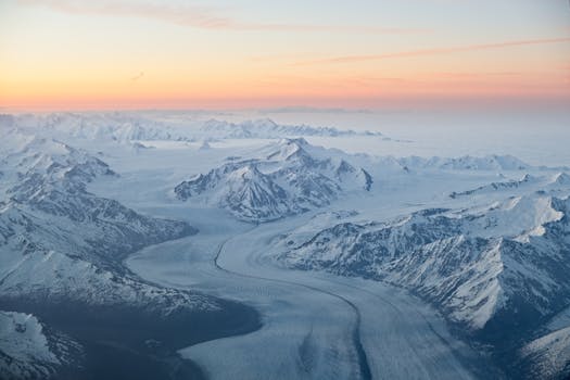 A breathtaking aerial view of the snow-covered mountains and glaciers in Alaska during sunset.