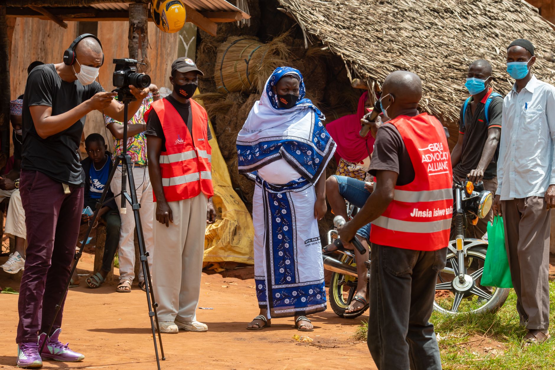 Researcher interviewing local cultural participants beside a community hall, notebooks and recorded stories visible