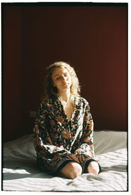 A serene woman in a floral robe sits on a bed, basking in sunlight.