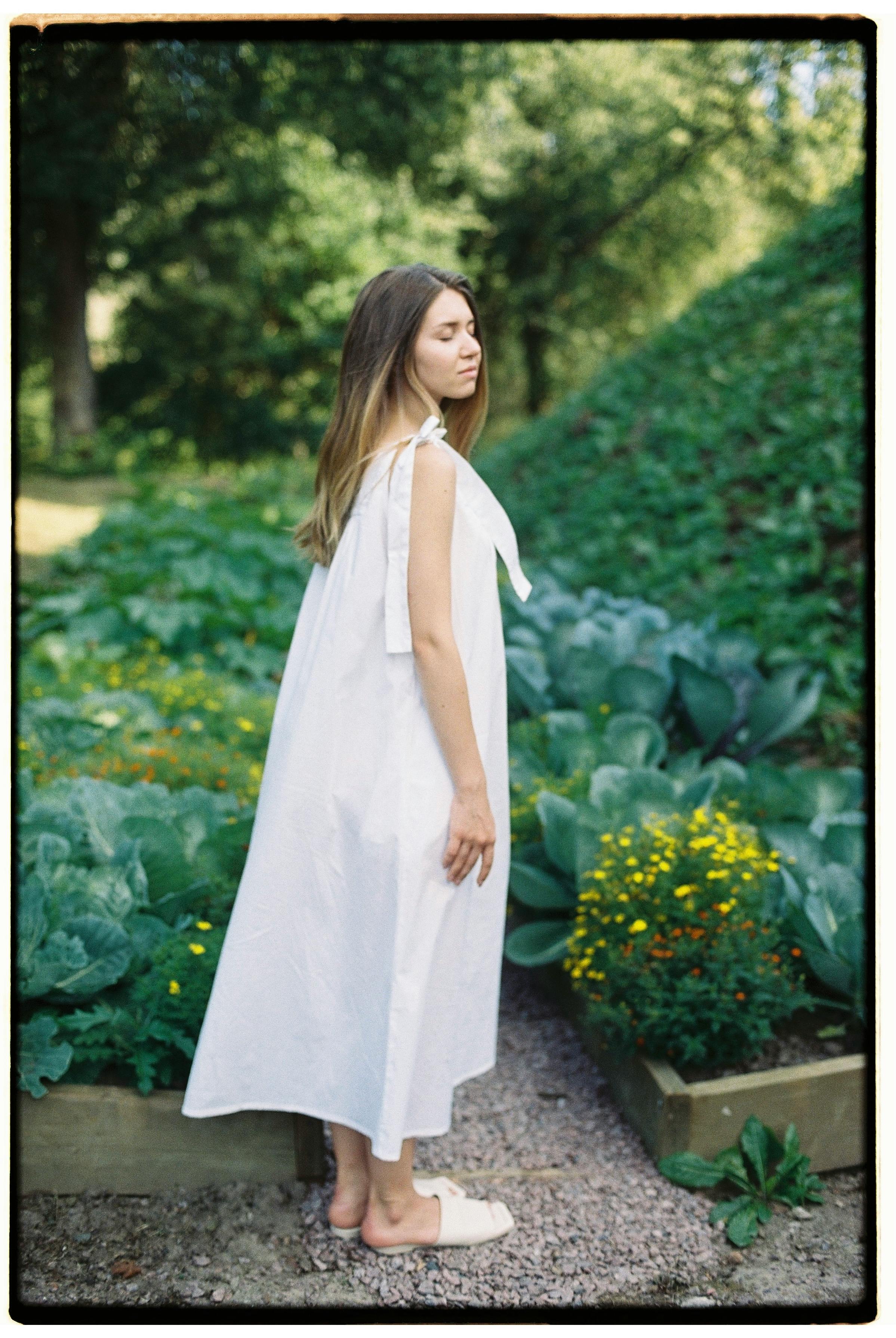 Woman stands gracefully in a blooming summer garden, embodying tranquility and nature.