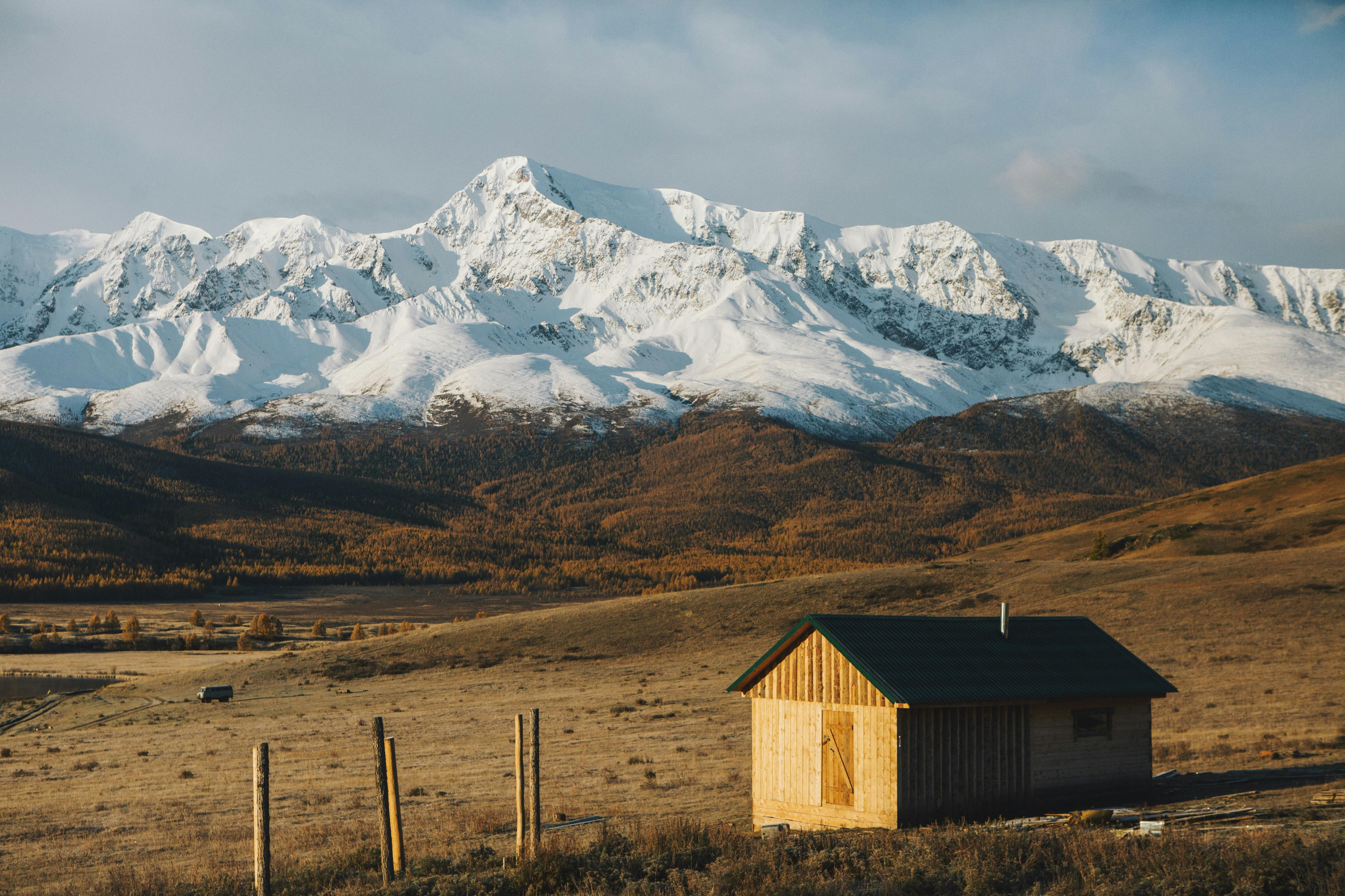 A serene view of a rustic cabin with snowy mountain peaks in the background, ideal for tranquil nature scenes.