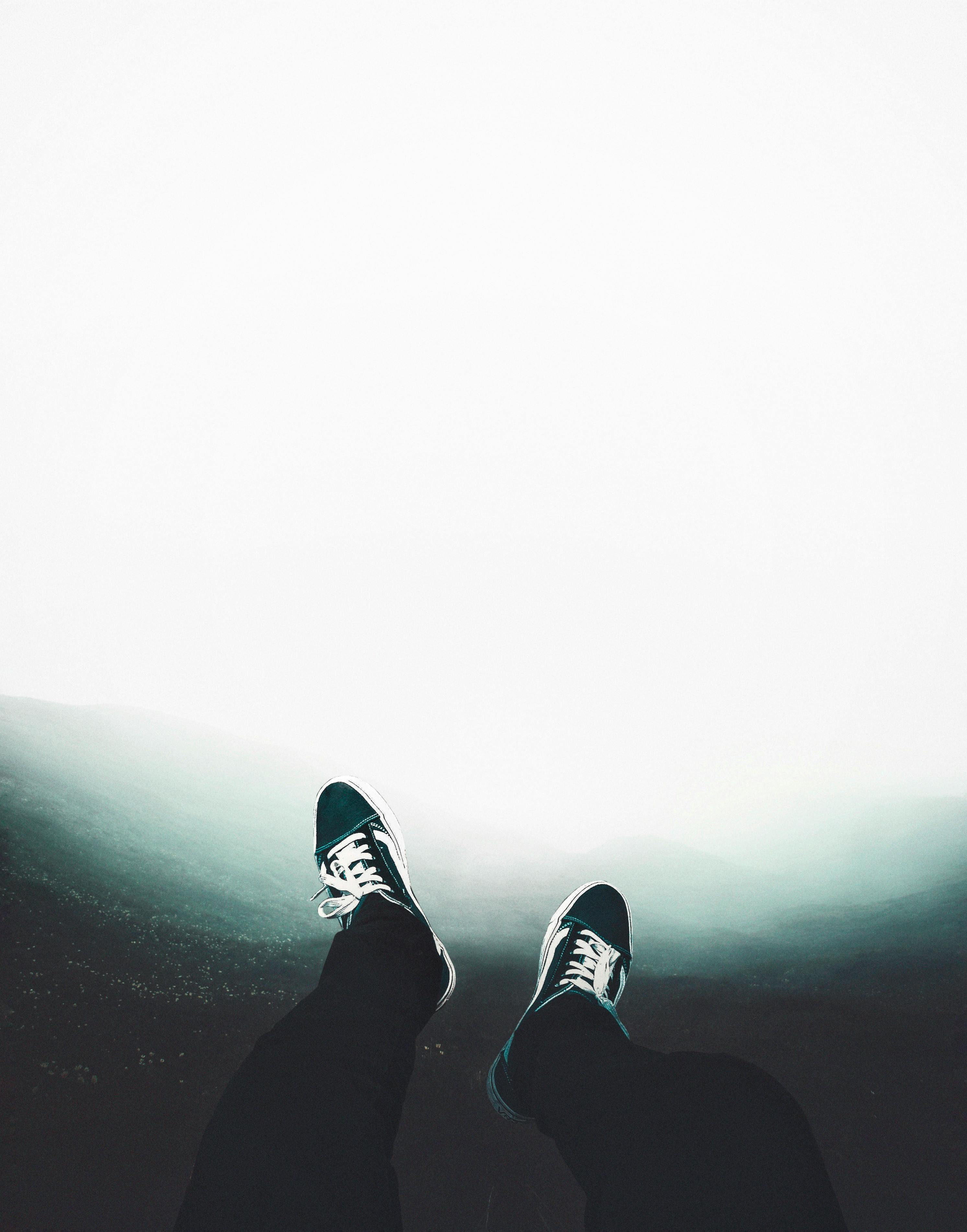 从鸟瞰视角看去，一双穿着运动鞋的腿悬在薄雾笼罩的山地景观之上