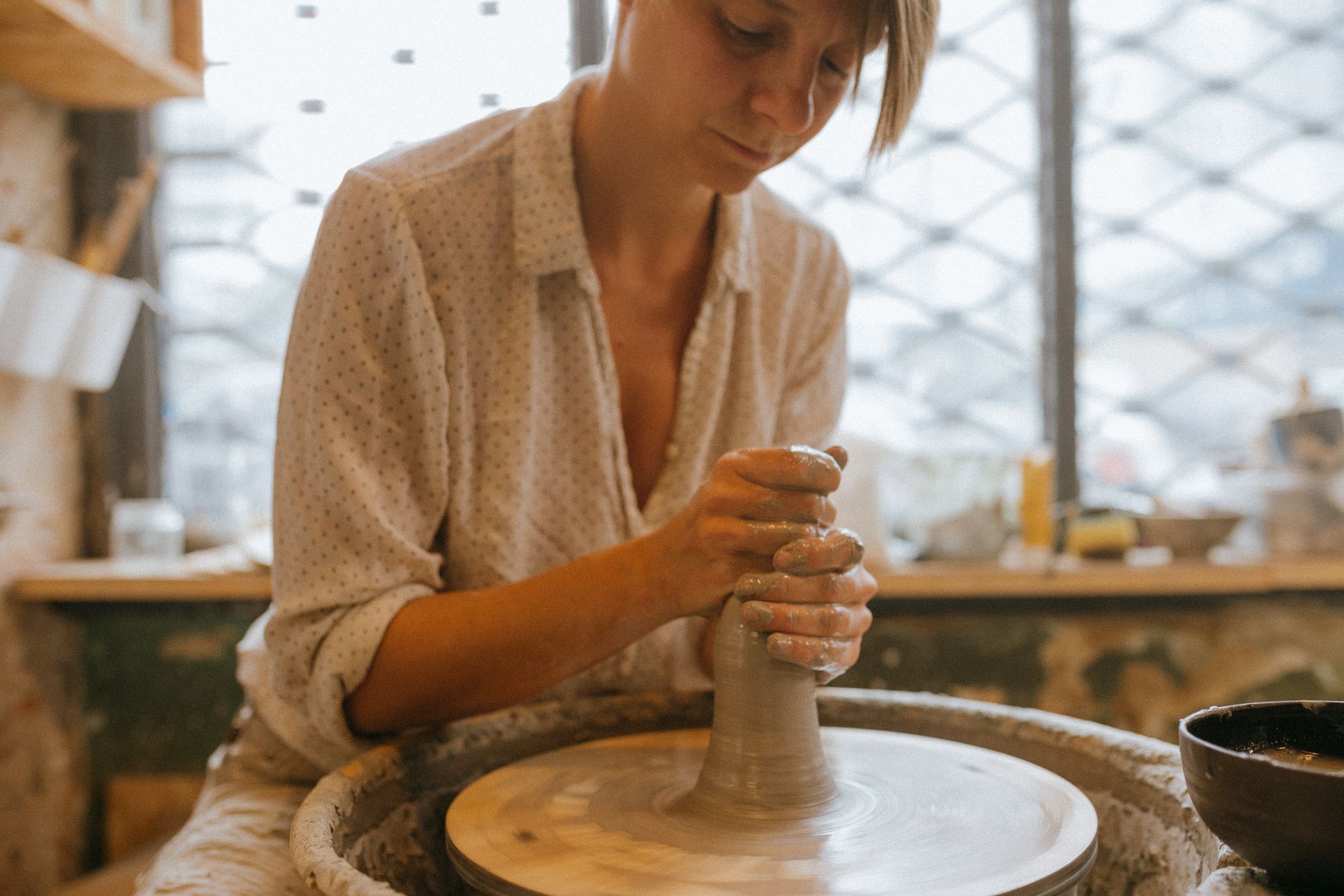 Focused woman shaping clay on a pottery wheel in a cozy ceramic workshop.
