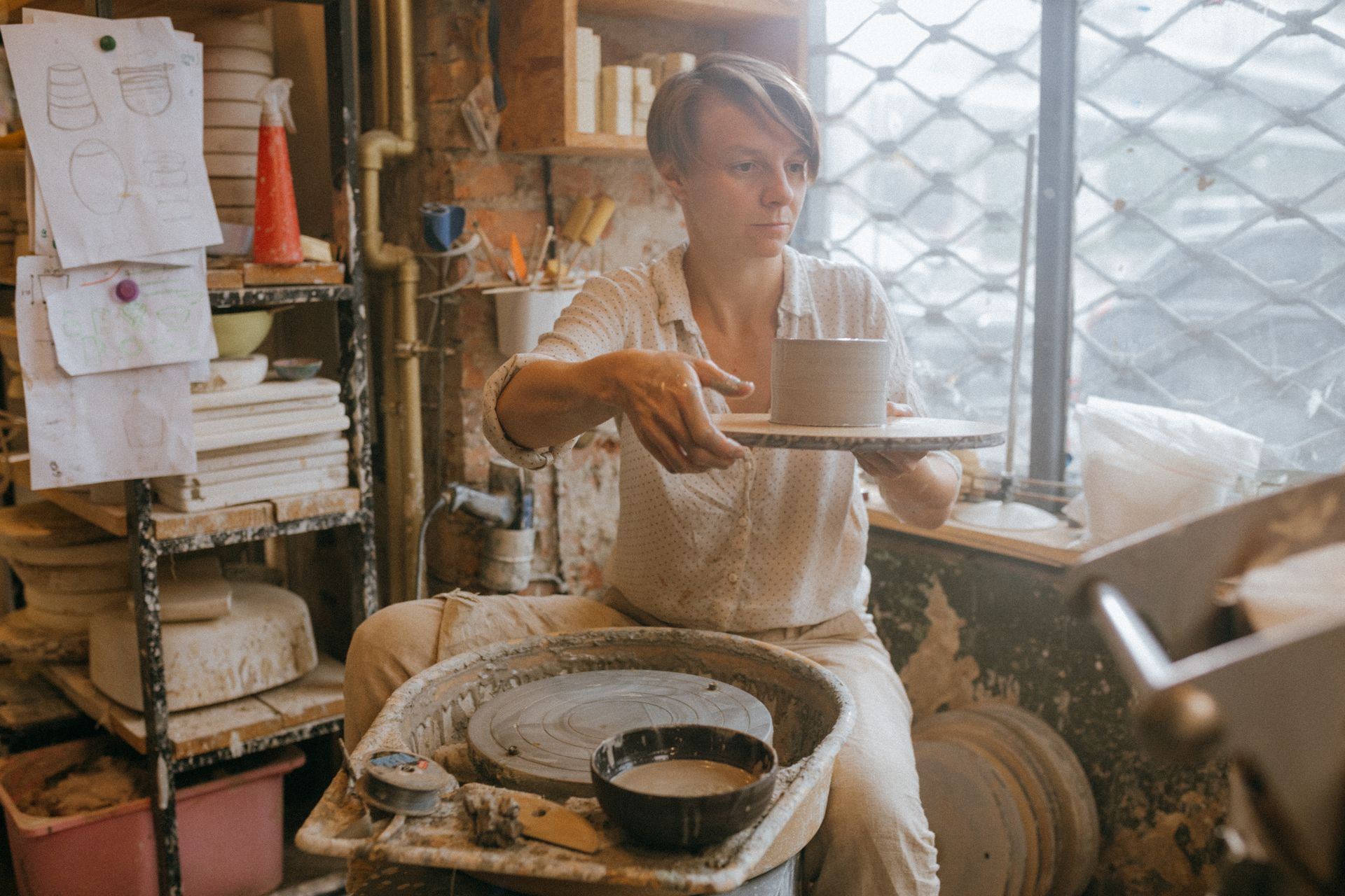 A focused artisan crafting pottery on a wheel in a ceramic workshop setting.