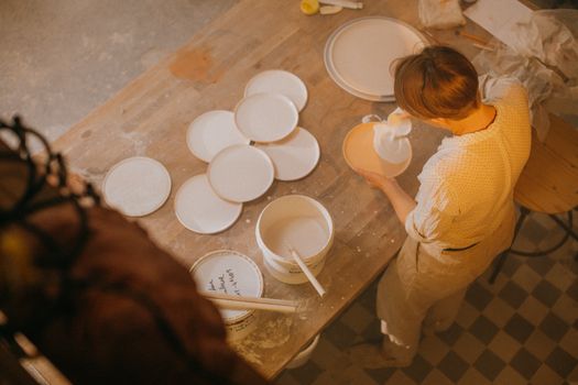 Woman glazing ceramic plates in an artistic pottery workshop, captured from above.