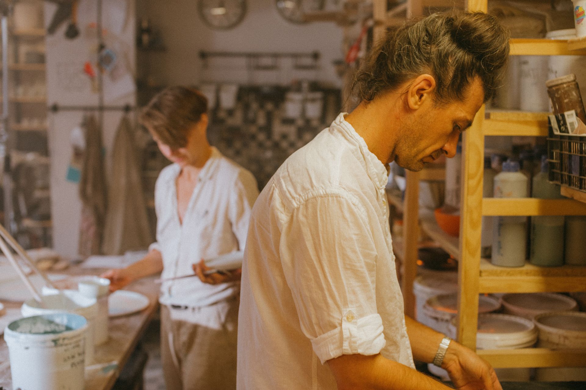 Two artisans at work in a cozy ceramic studio creating pottery with precision and care.