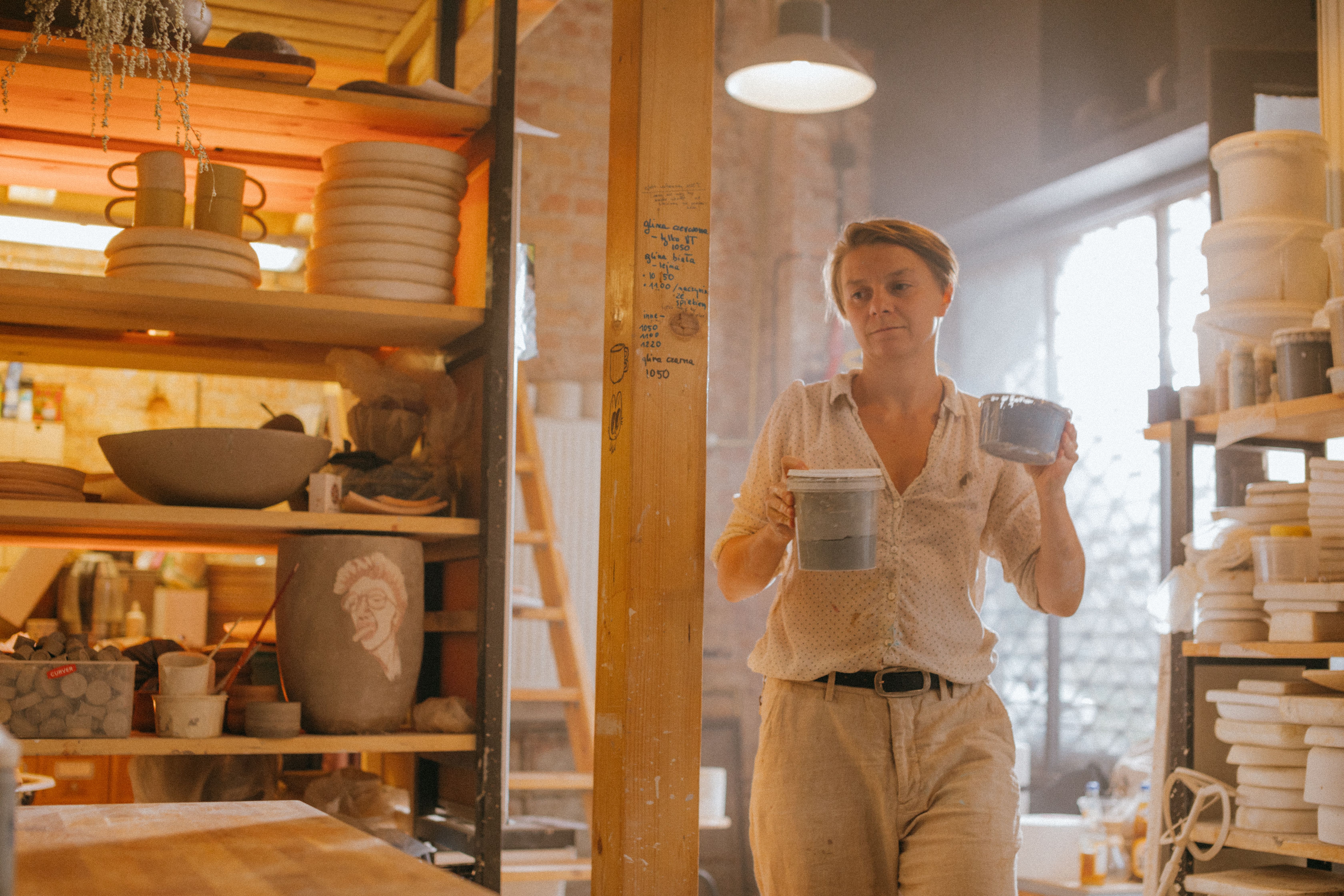 A woman artist holding ceramic bowls in a sunlit workshop