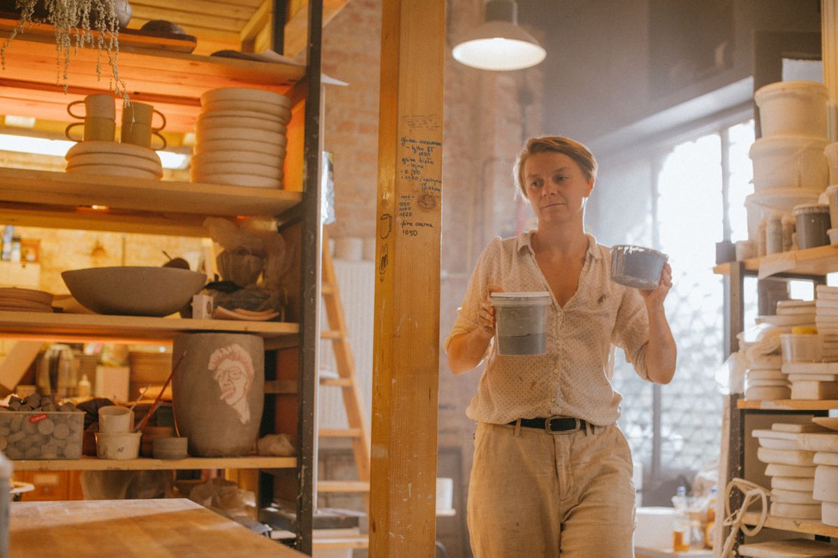 A maker carrying two finished ceramic bowls through the sunlit studio