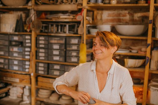 A smiling artisan in a pottery workshop surrounded by tools and shelves, creating ceramic art.