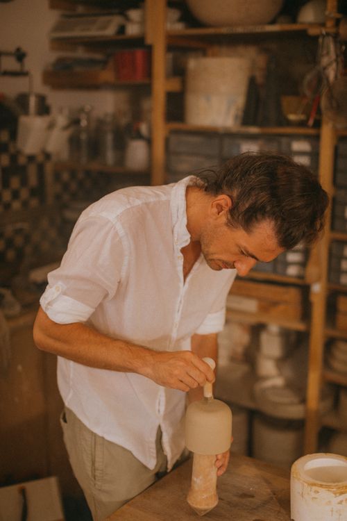 Free Male artisan meticulously crafts a ceramic vase in a pottery workshop filled with tools and materials. Stock Photo