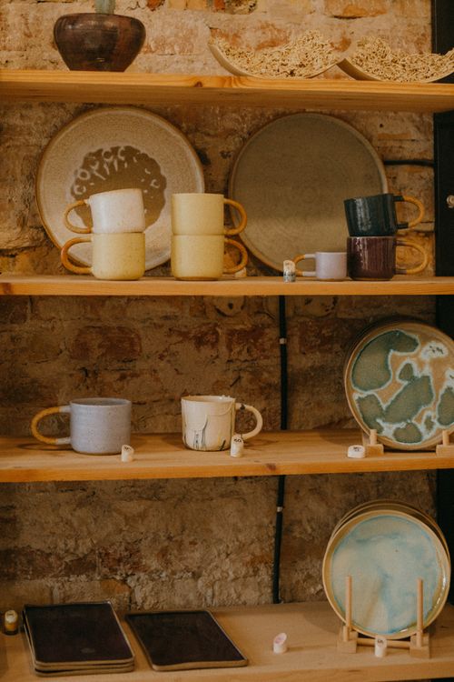 Free Vibrant ceramic dishware displayed on rustic wooden shelves in workshop setting. Stock Photo
