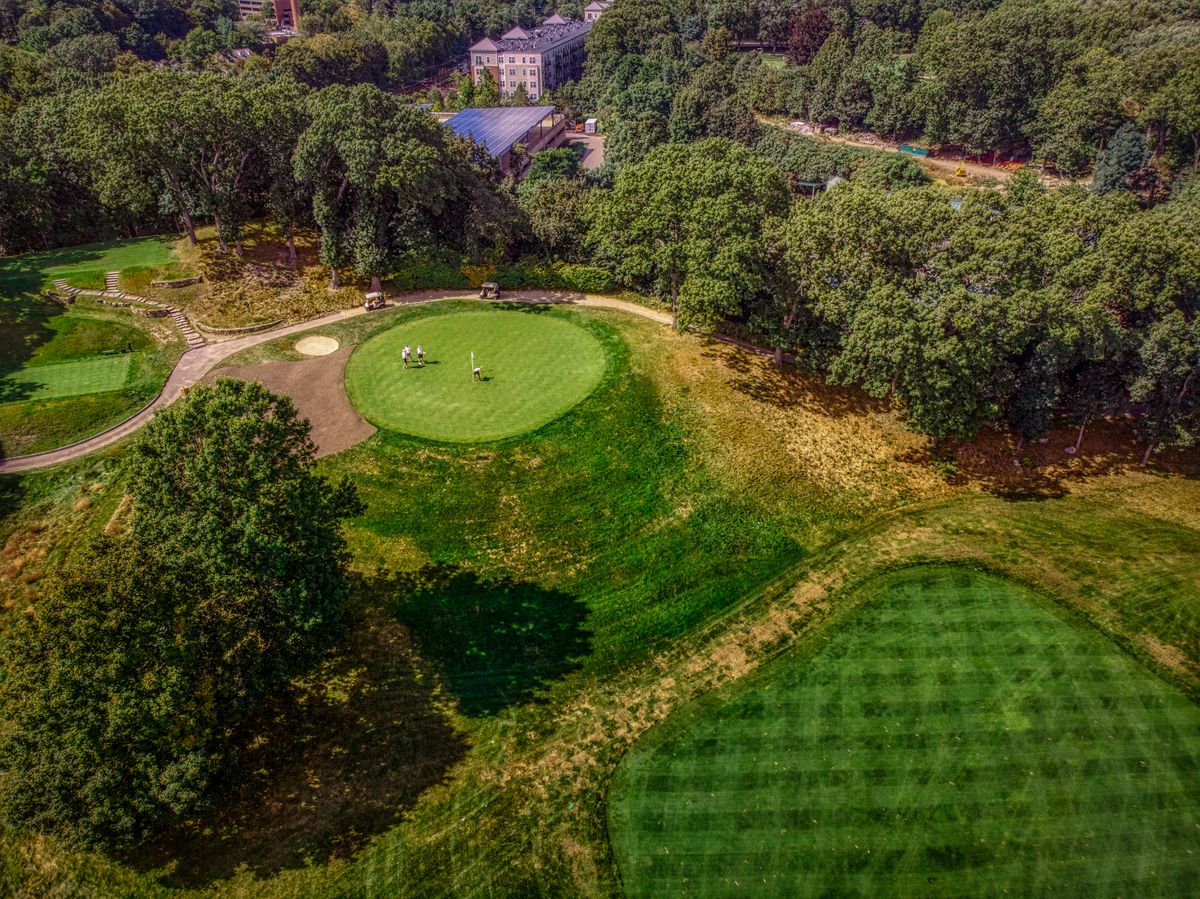 Aerial view of a lush golf course surrounded by trees under a sunny sky