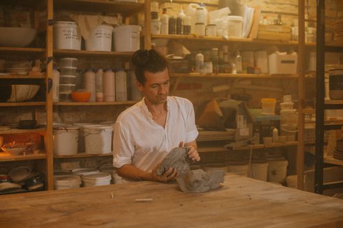 Free An artisan skillfully sculpts clay in a warm, inviting workshop brimming with pottery supplies. Stock Photo