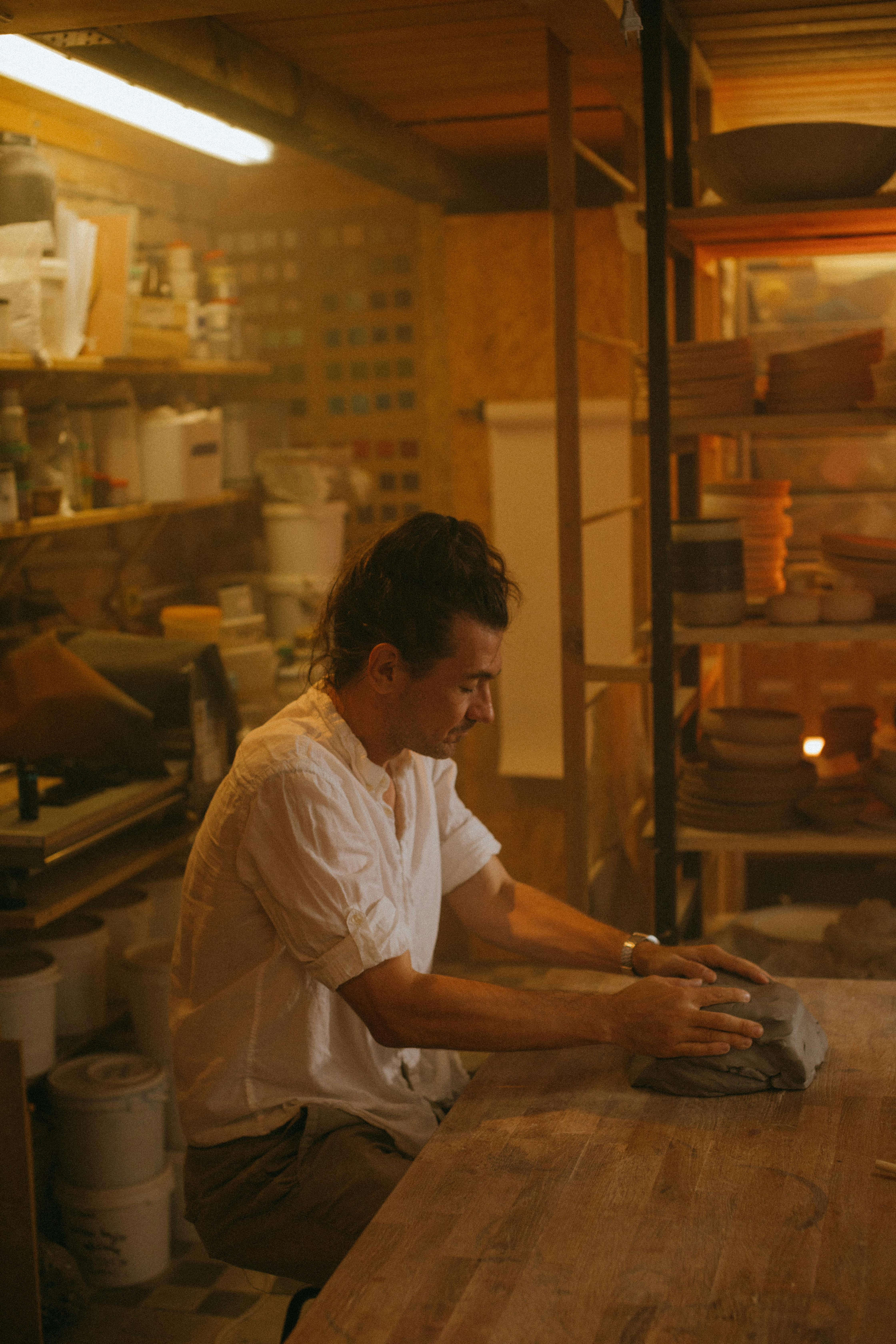 An artisan shaping clay with focused precision in a cozy, dimly-lit workshop.