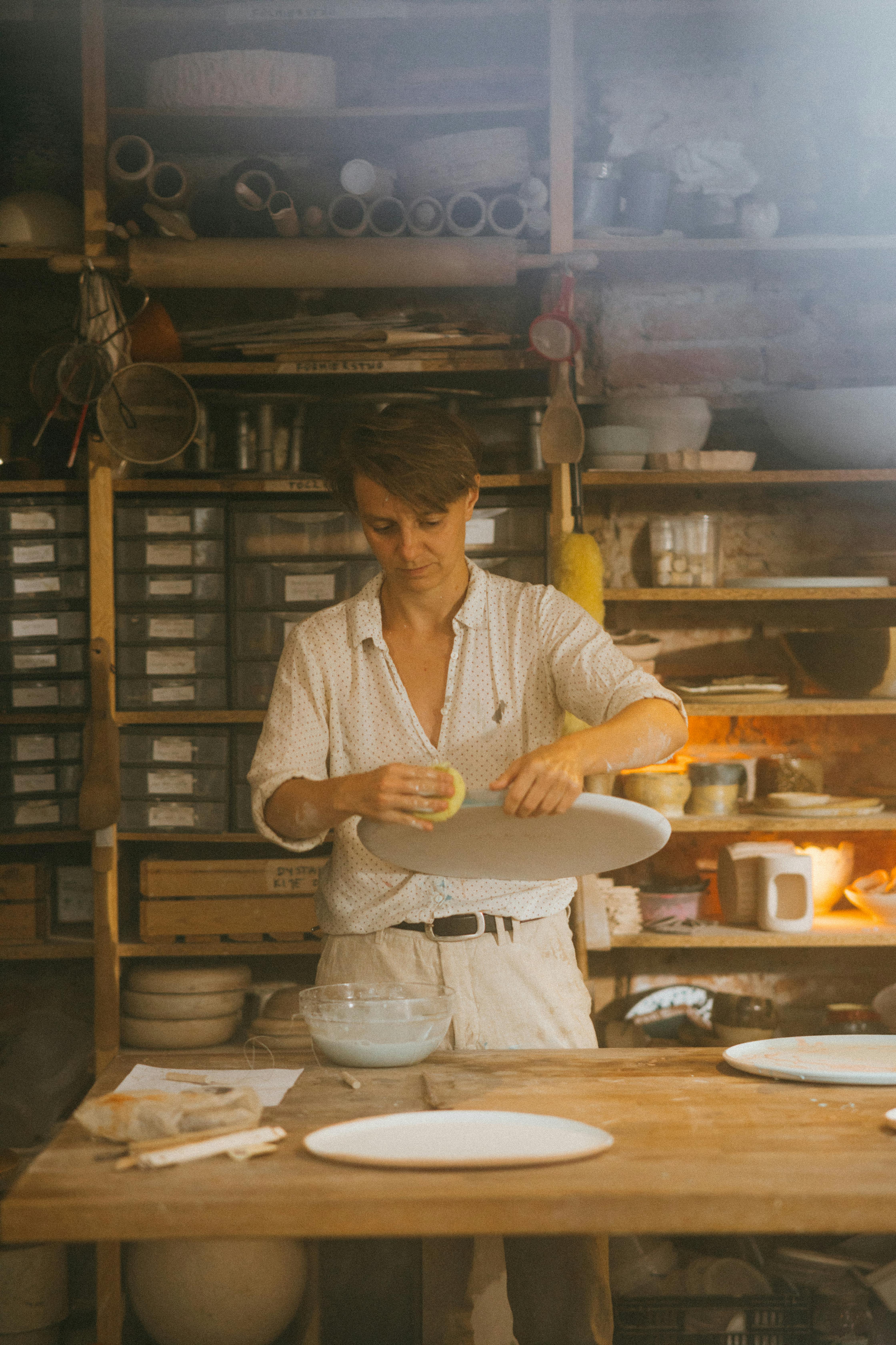 A skilled potter shaping ceramics in a sunlit workshop filled with crafting tools and pottery pieces.