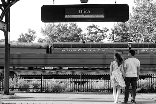 Grayscale Photo of a Couple Holding Hands While Standing Near Train Rail