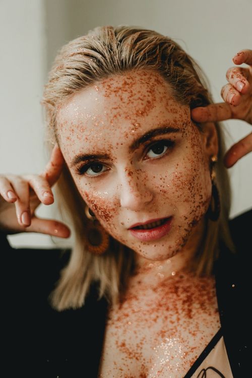 Free A captivating artistic portrait of a woman indoors with glitter on her face and holding her head. Stock Photo