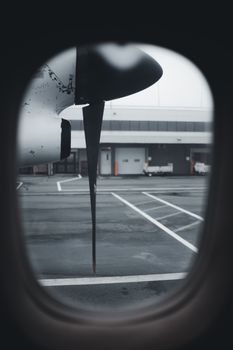 Close-up of a propeller seen through an airplane window on a cloudy day at the airport.