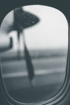 Atmospheric monochrome view through airplane window on a rainy day, capturing raindrops and distant landscape.