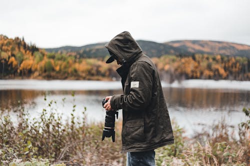 Side View of a Man Holding a Camera while Standing Near a Lake