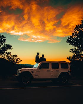 Silhouette of a couple on a Jeep, enjoying a vibrant sunset on a scenic adventure.