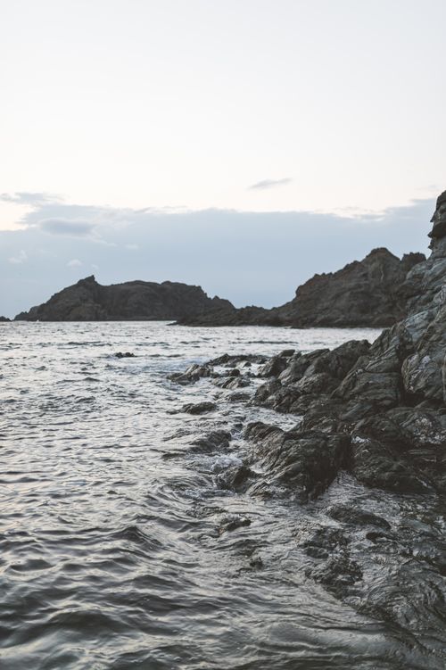 Free Serene rocky coast with ocean waves and a dusky sky, perfect for seashore scenes. Stock Photo