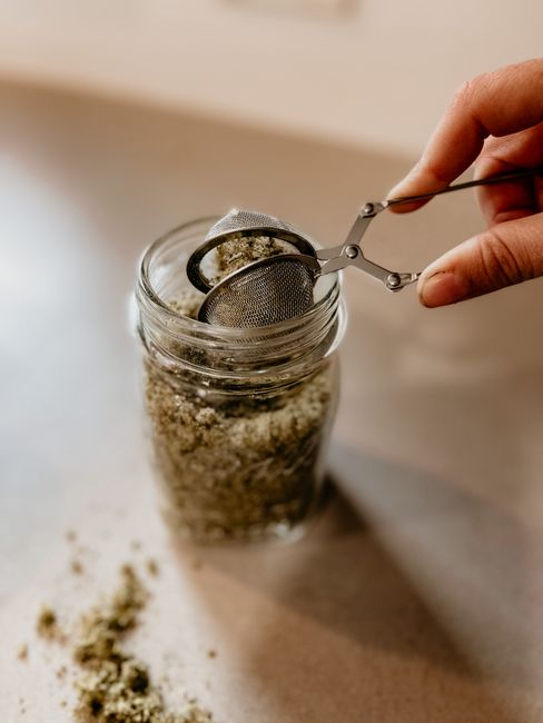 Hand opening a glass mason jar containing herb-infused oil`