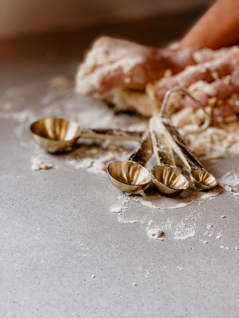 Close-up of hands kneading dough with vintage measuring spoons and flour on a countertop.