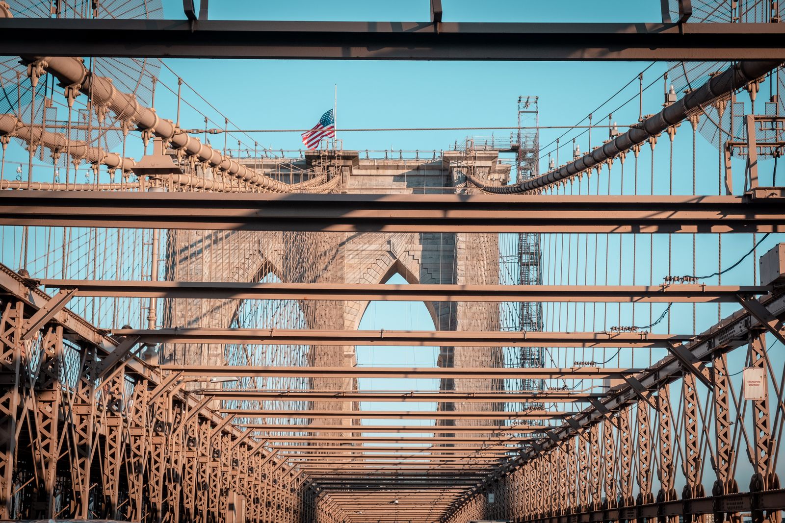 The Brooklyn Bridge's cables against a clear sky with a flag
