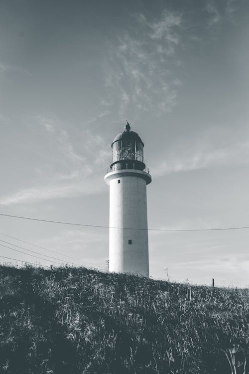 Grayscale Photo of a Lighthouse on a Grassy Field