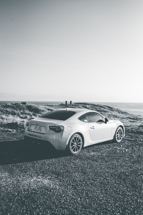 Free A sleek sports car parked by a scenic coastal road in monochrome tones. Stock Photo