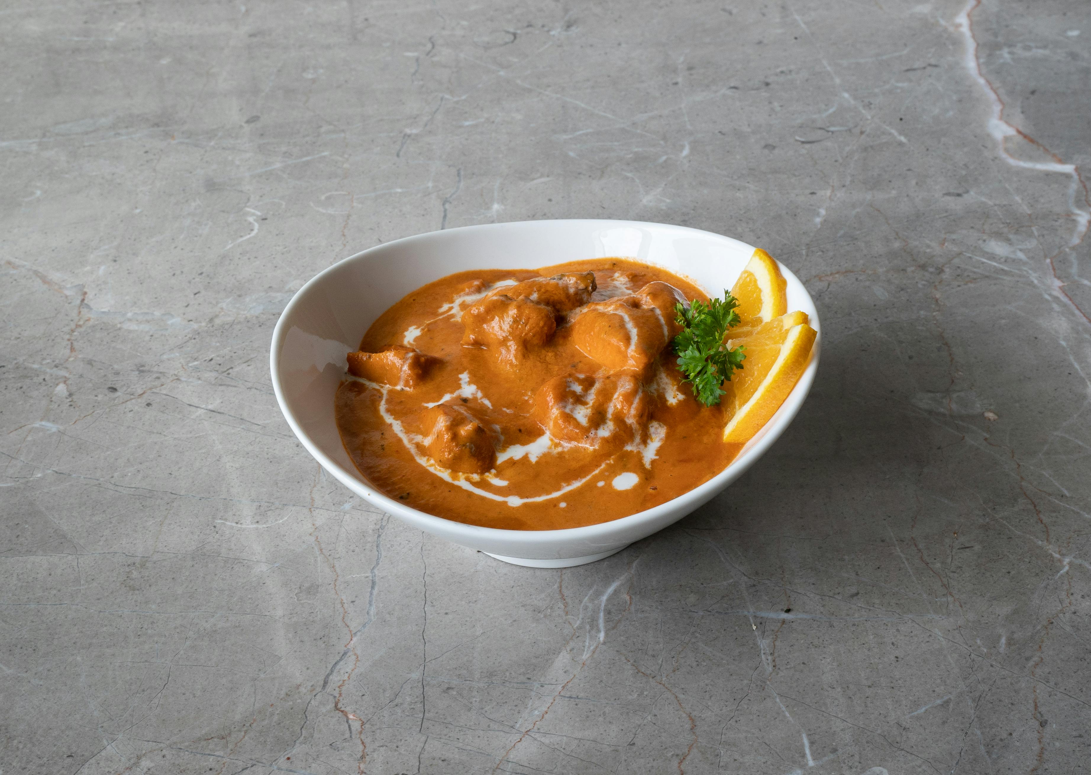 A savory bowl of butter chicken garnished with fresh herbs and citrus slices.