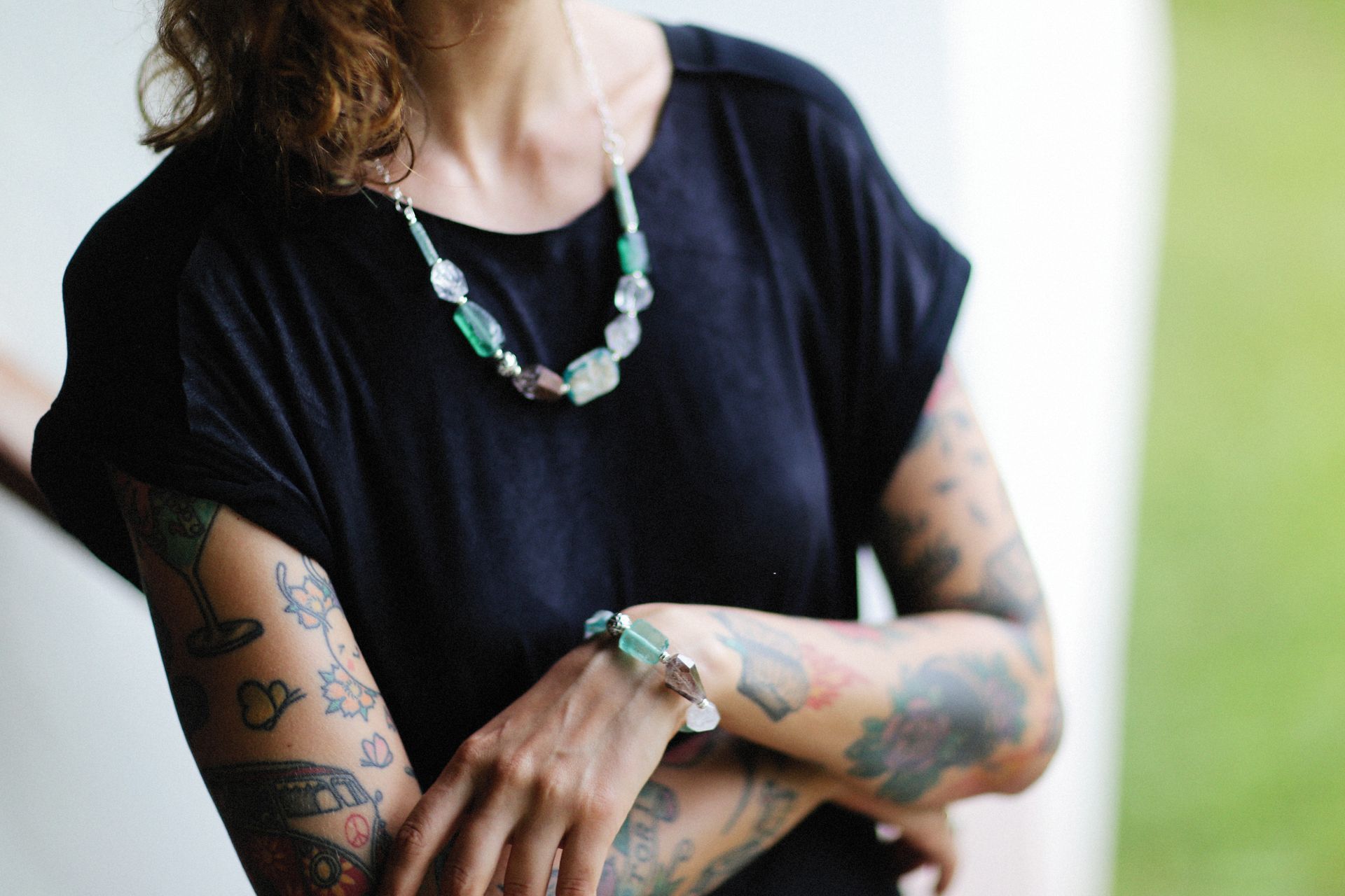 Close-up of a tattooed woman's arms and jewelry, featuring intricate tattoos and gemstone accessories.