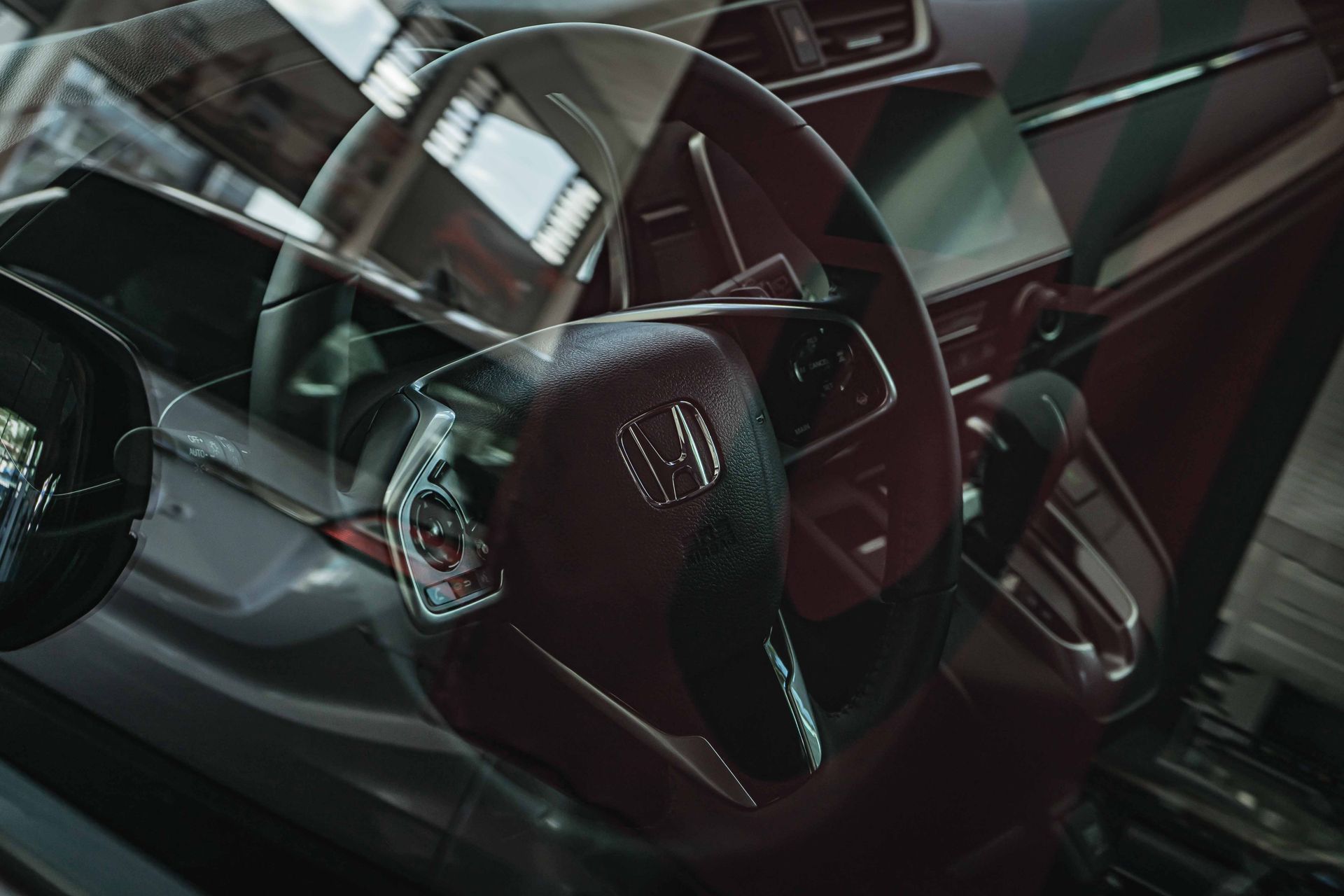 Close-up of a Honda car interior highlighting the steering wheel through a reflective glass view.