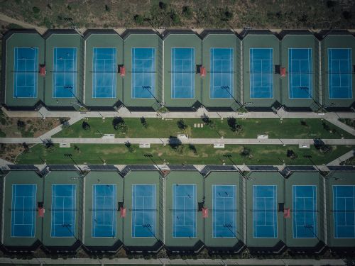 Free Drone view showcasing aligned tennis courts with clear pathways and greenery. Stock Photo