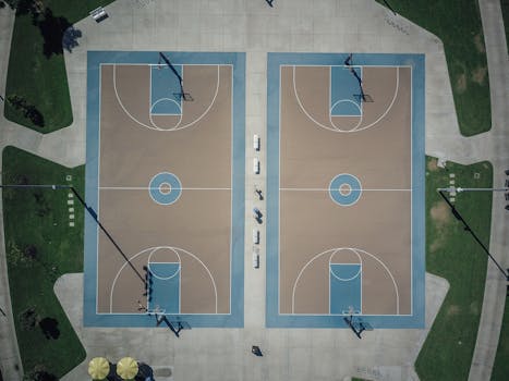 Drone shot of twin outdoor basketball courts surrounded by greenery.
