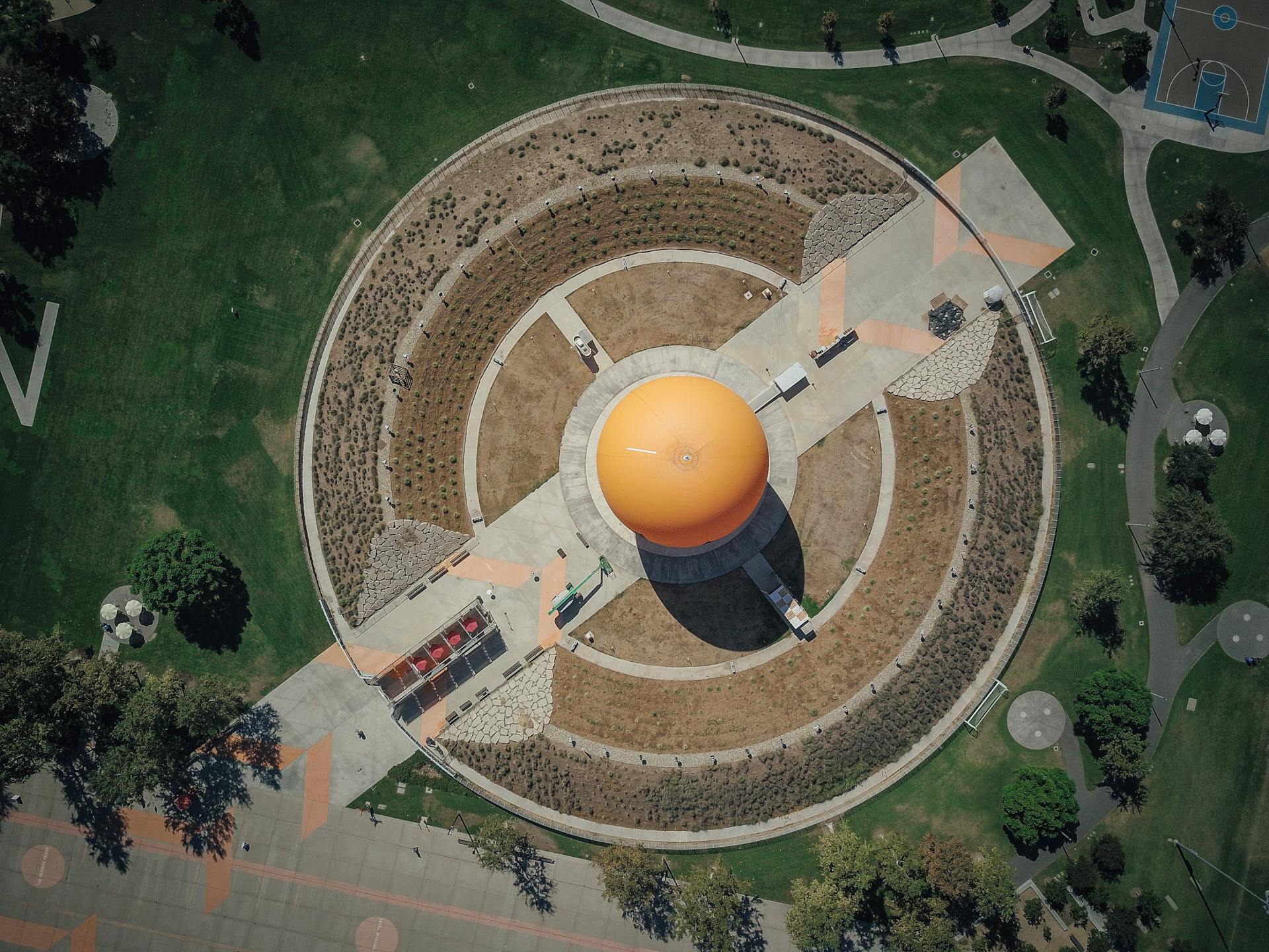 Aerial view capturing an orange dome structure surrounded by greenery and pathways in a city park.