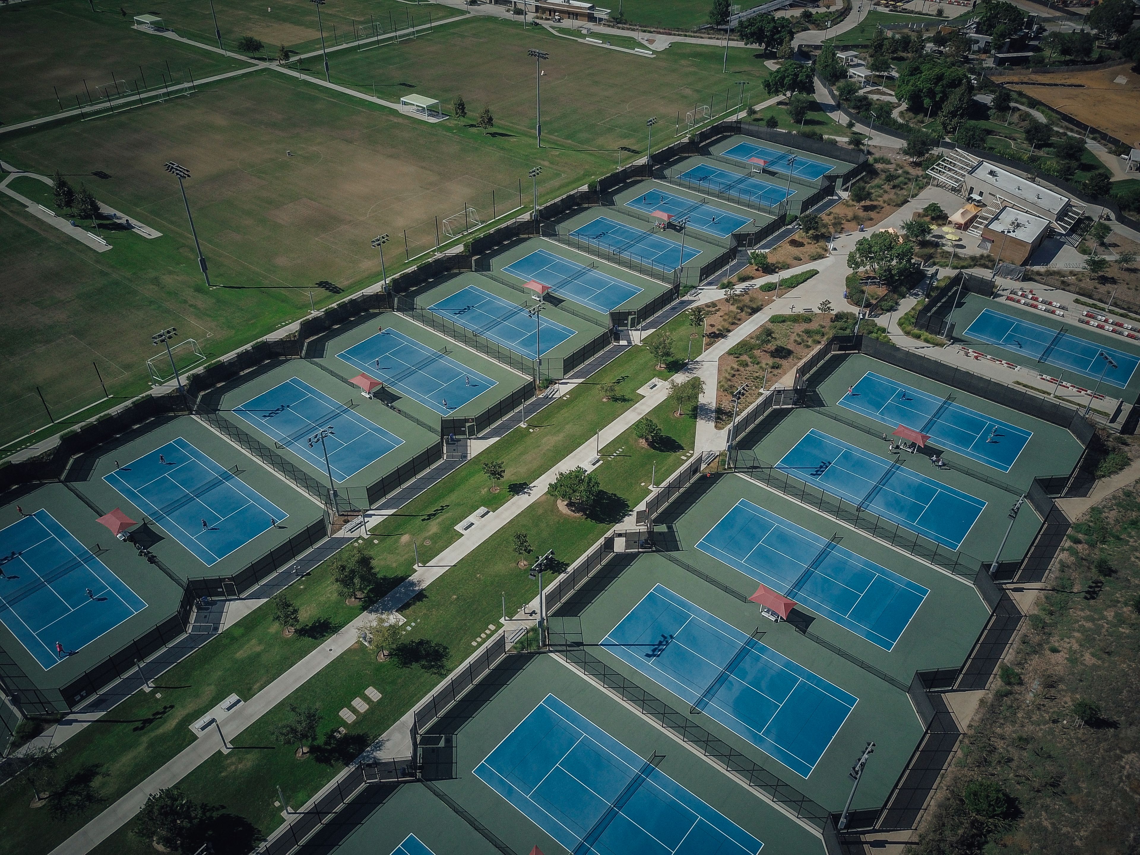 Aerial shot of numerous tennis courts in a recreational park during the day.