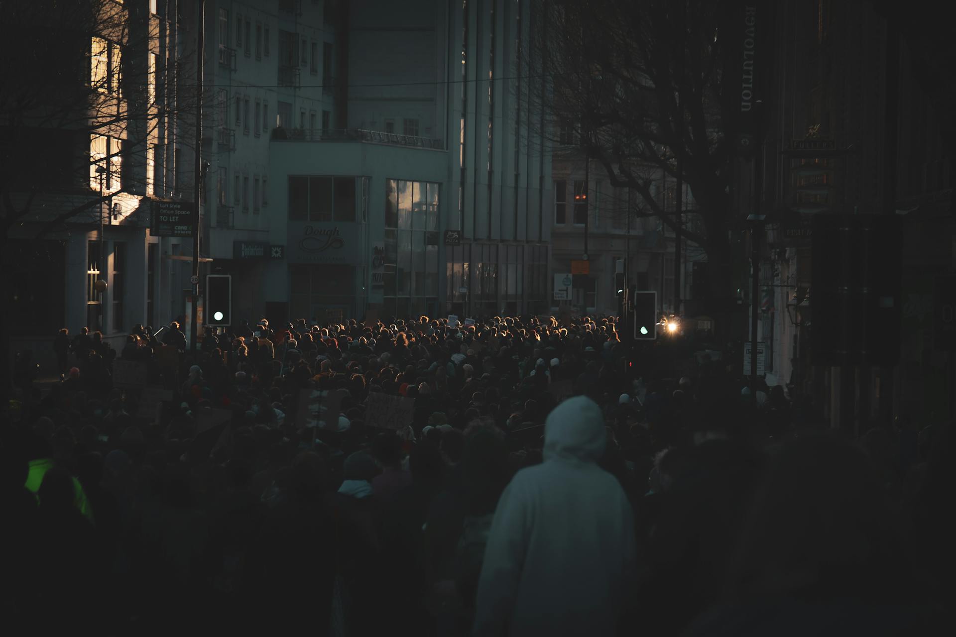 A large crowd gathers for a protest rally on a dimly lit street in Bristol, England.