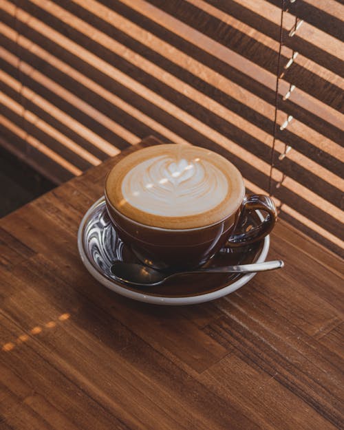 Free Latte Art Cup with Saucer on Brown Wooden Table Stock Photo