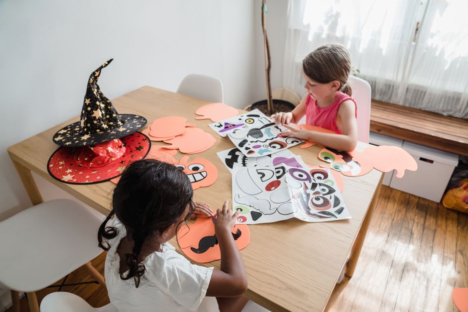 テーブルで紙と魔女の帽子を使ってハロウィンのクラフトを作っている二人の子供。