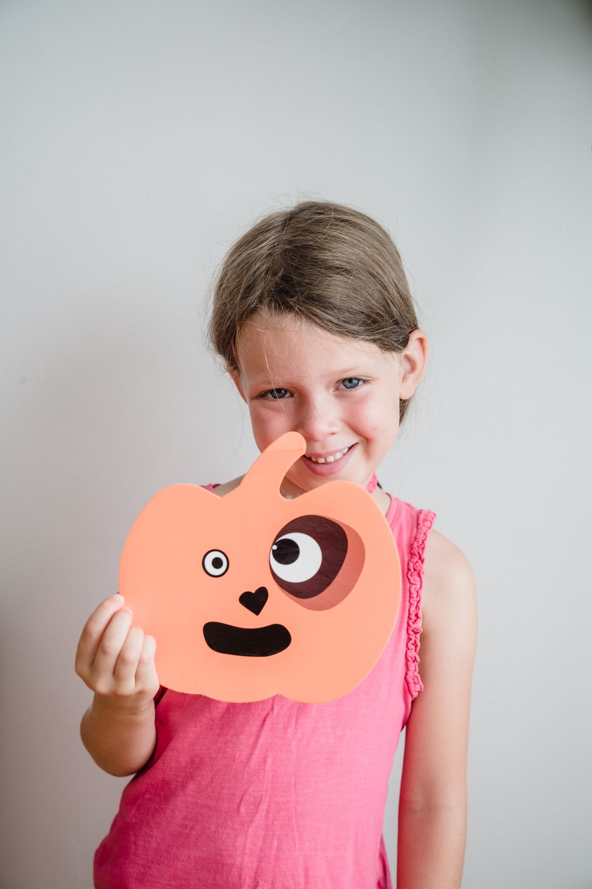 Smiling girl holding a pumpkin face made from orange and black paper