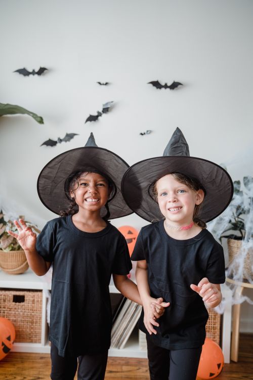 Free Two kids smiling in witch costumes celebrating Halloween indoors. Festive and fun ambiance. Stock Photo